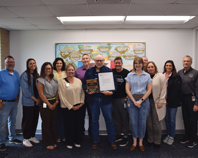 Delbert Longley holding his award and Governor's letter surrounded by DOC Central Office staff